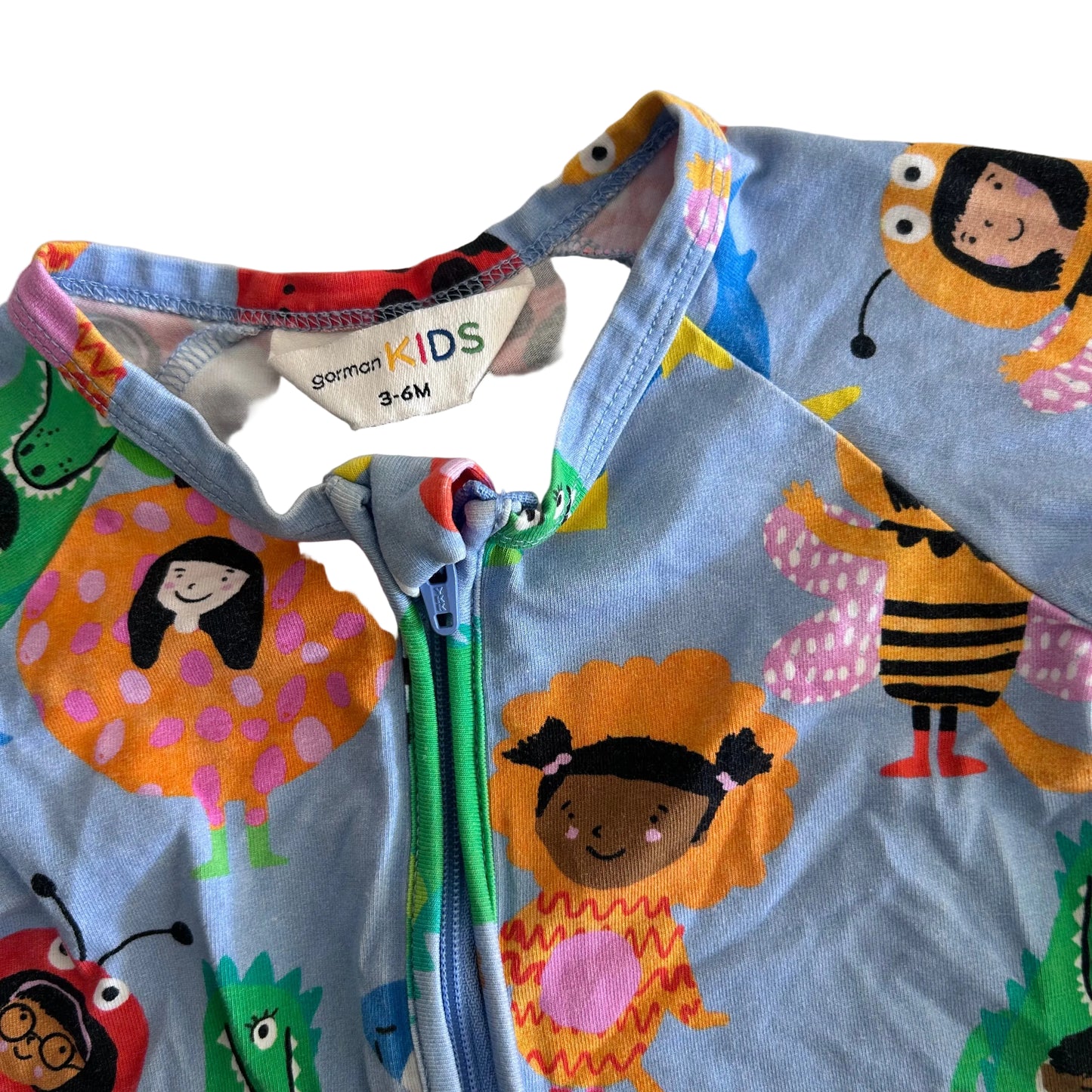 A close-up of a children's zip-up one-piece outfit in light blue, featuring a colorful cartoon print of children, bees, and insects. The brand label 'Gorman KIDS' is visible inside the collar.