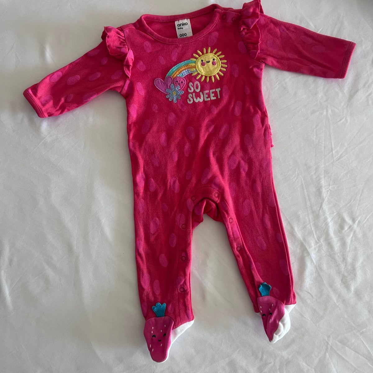 Anko Age 000 long sleeved onesie in hot pink with polka dot with embroidered rainbow, sun, butterfly and flower appliqué, 'so sweet' text, ruffle shoulder detail, strawberry character feet — gently loved condition.