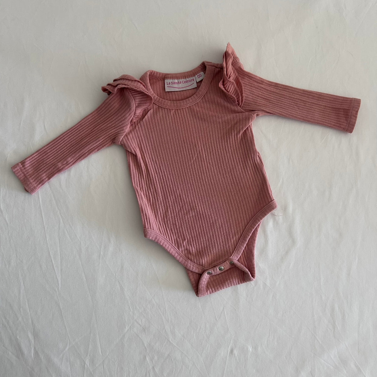 La Sienna Couture Age 00 long sleeve ruffle shoulder bodysuit in dusty pink/mauve with ribbed texture with ruffle shoulder detail, gently loved condition.