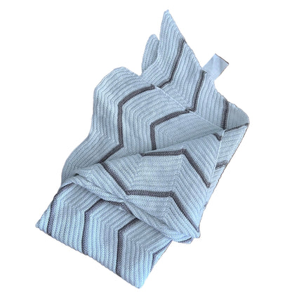 A folded woven blanket with a gray chevron pattern on a white background, placed on a background.