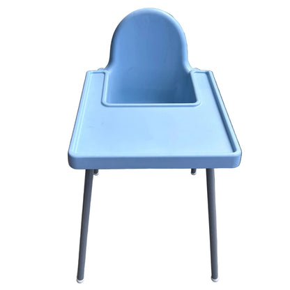 A light blue plastic baby high chair with a tray and silver metal legs, photographed outdoors on a tiled patio against a white wall.