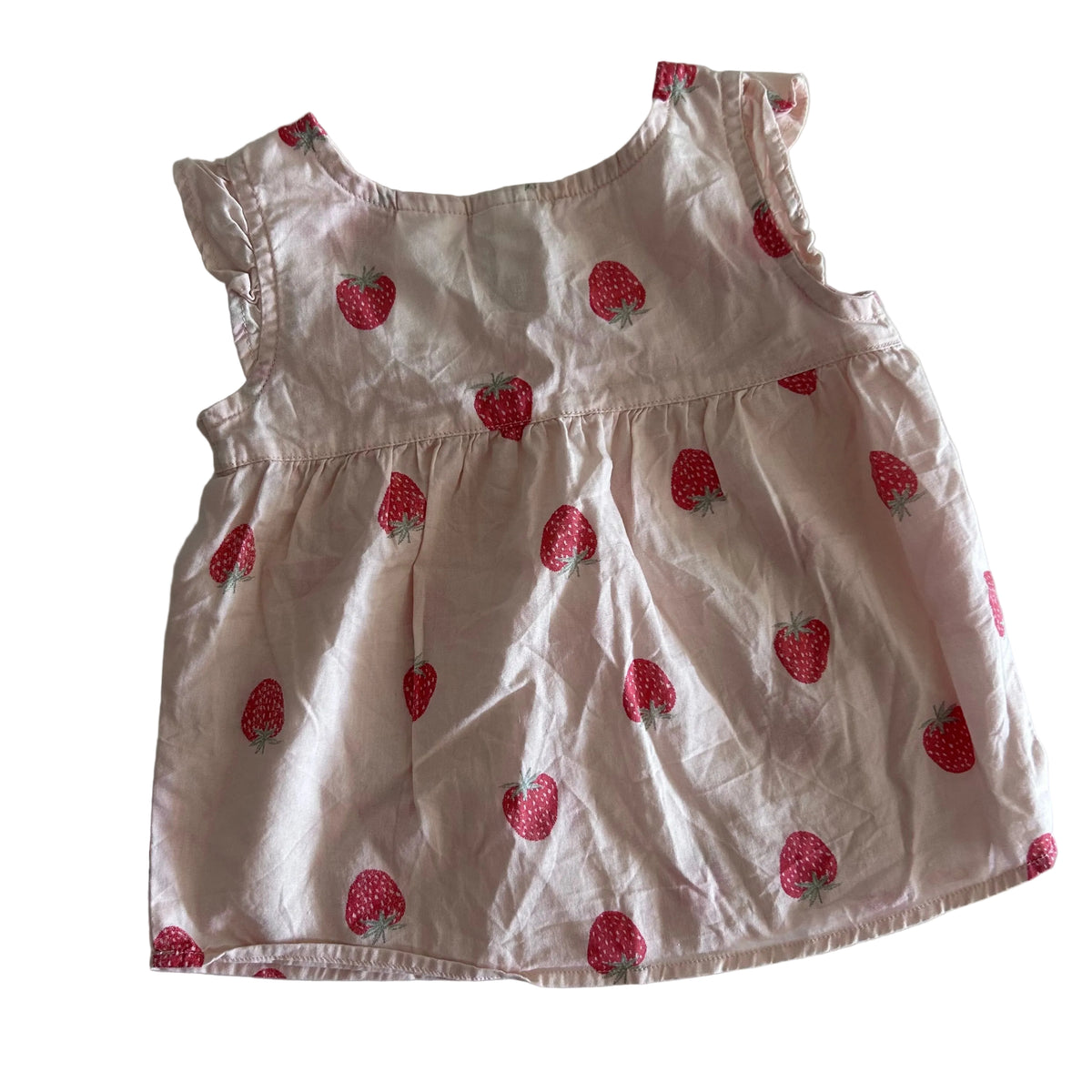 A sleeveless baby dress in light pink fabric with a red strawberry print, laid flat on a white sheet.