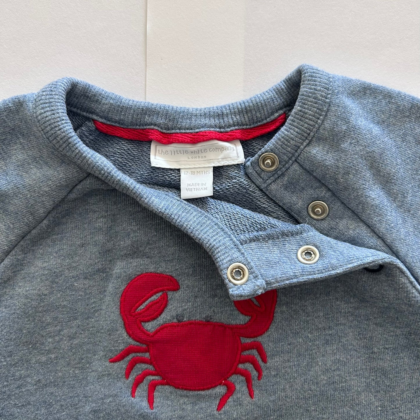 Blue-grey sweater with red crab design and visible brand label on a light gray background