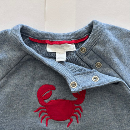 Blue-grey sweater with red crab design and visible brand label on a light gray background