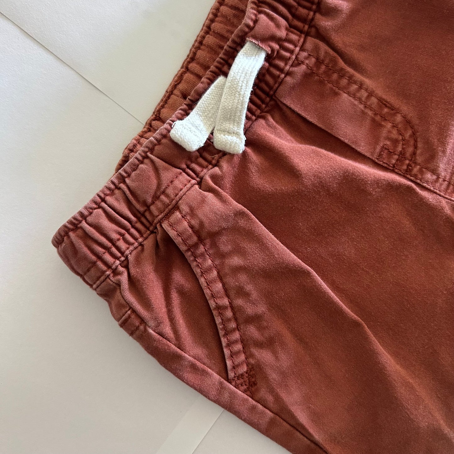 Close-up of red-brown trousers with cream-white drawstring on a light background