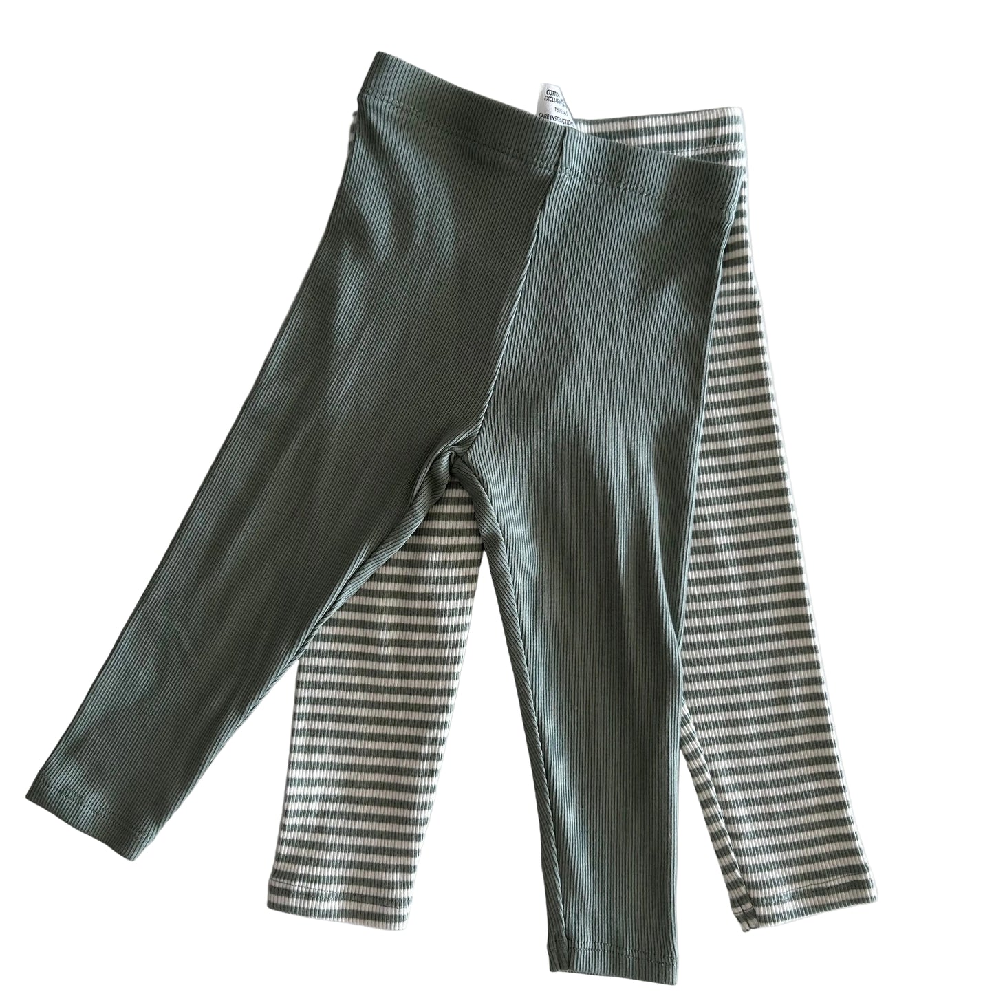 Green ribbed leggings on top of striped leggings on a light background