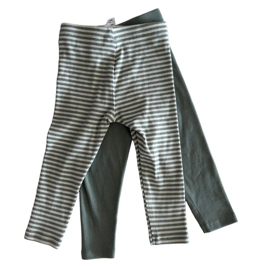 Two pairs of green themed baby leggings on a light surface