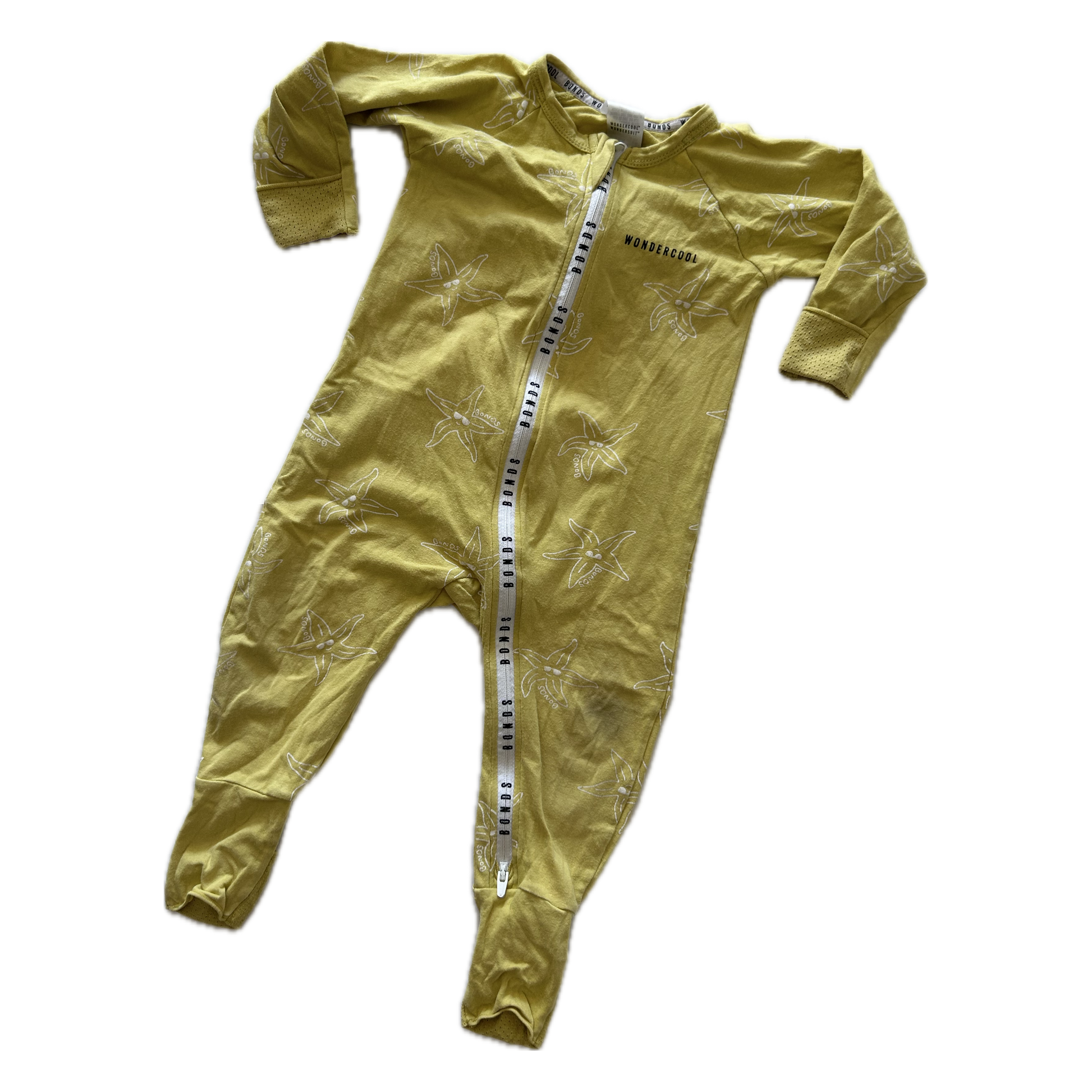 A baby's long-sleeve footed sleeper in a muted mustard yellow color, featuring a subtle tonal palm tree pattern and a white zipper with black Bonds lettering down the front