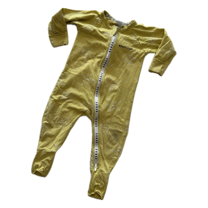 A baby's long-sleeve footed sleeper in a muted mustard yellow color, featuring a subtle tonal palm tree pattern and a white zipper with black Bonds lettering down the front