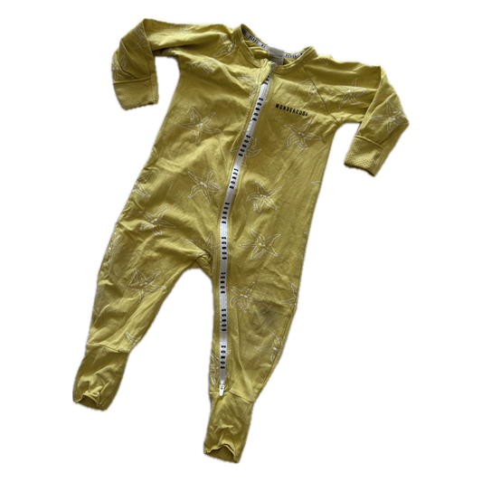 A baby's long-sleeve footed sleeper in a muted mustard yellow color, featuring a subtle tonal palm tree pattern and a white zipper with black Bonds lettering down the front