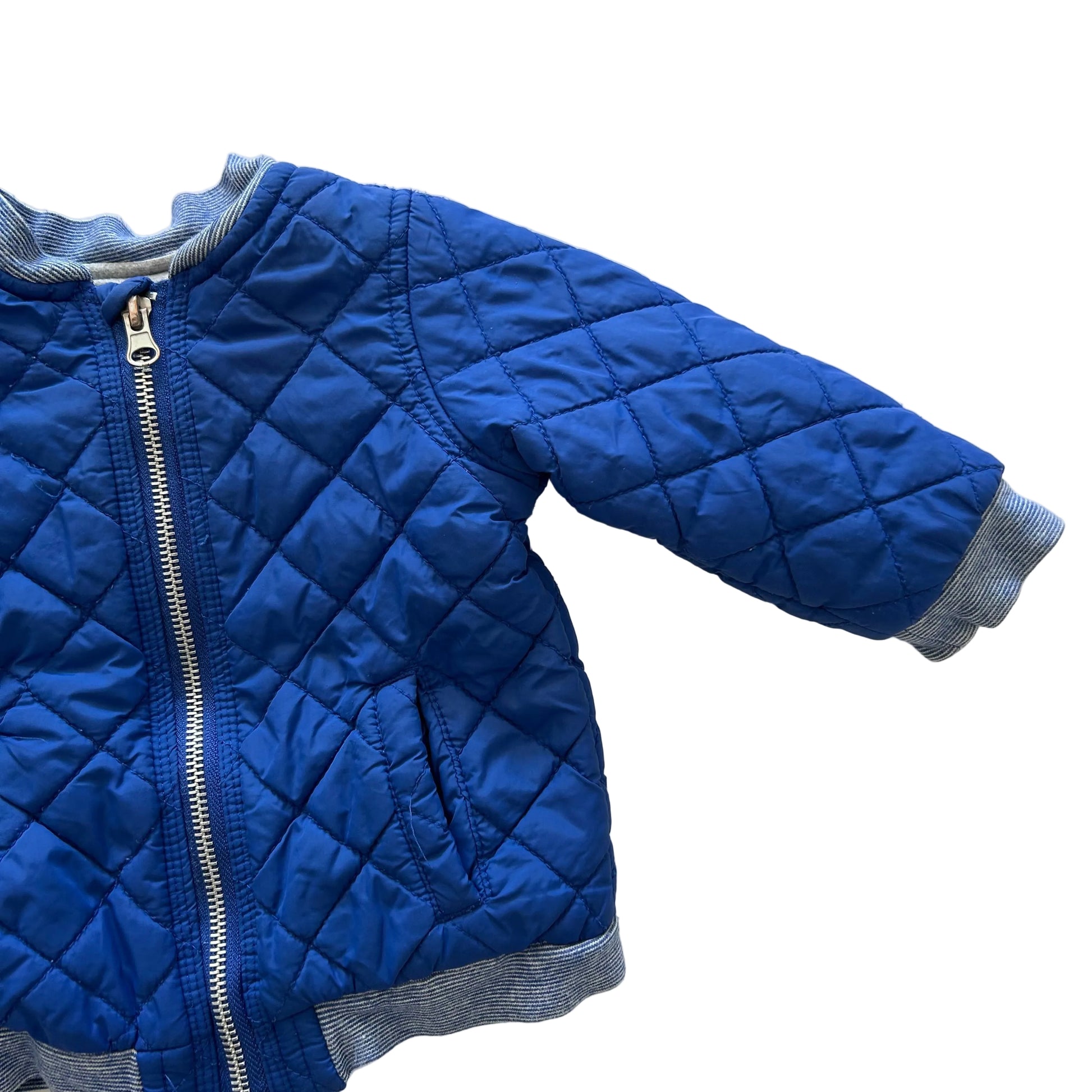 A blue quilted jacket with diamond stitching, a silver zipper, and gray ribbed trim, laid flat on a white background.