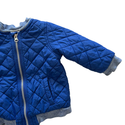 A blue quilted jacket with diamond stitching, a silver zipper, and gray ribbed trim, laid flat on a white background.