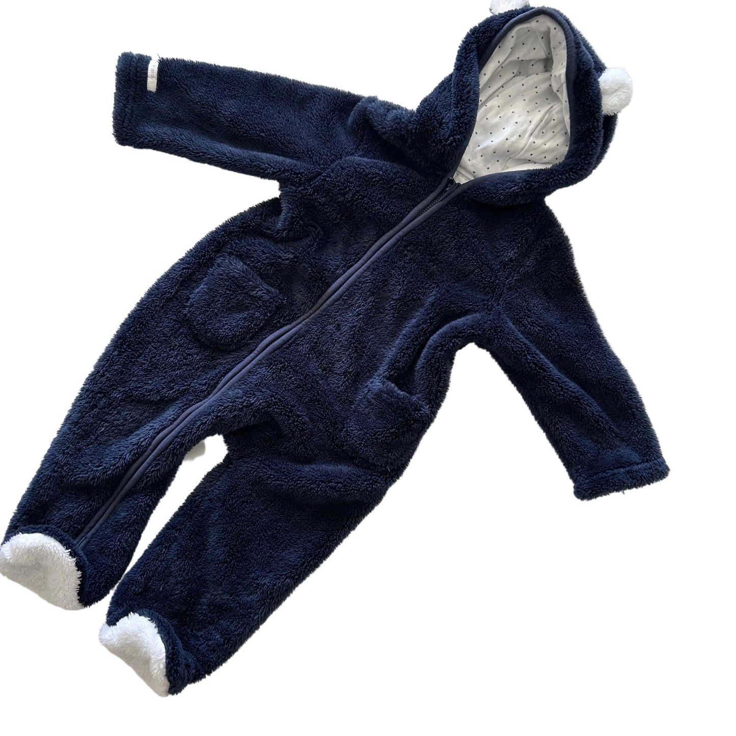 A navy blue fleece baby jumpsuit with white pom-pom details on the hood and white plush foot covers, laid flat on a white background.