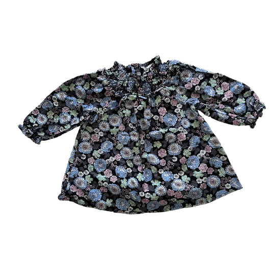 A long-sleeve blouse with a dense floral pattern in shades of blue, pink, and green on a black background, laid flat on a white background.