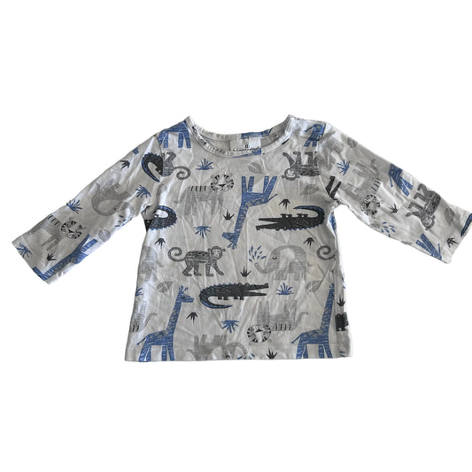 A long-sleeve baby t-shirt with a safari animal print featuring crocodiles, giraffes, and zebras in blue, gray, and black on a white background, laid flat on a light surface.