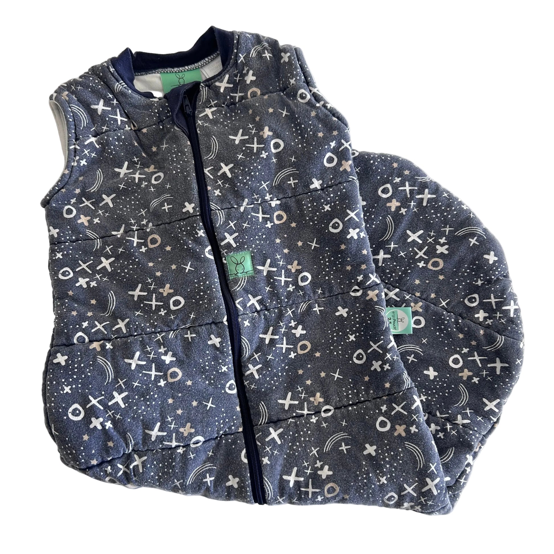 A sleeveless quilted sleeping bag laid flat on a white background, featuring a dark gray and navy blue space-themed print with stars, moons, and a white-and-black tic-tac-toe pattern. 
