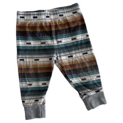 The front of pair of children's striped trousers with horizontal bands of brown, green, grey, black, and white, featuring ribbed ankle cuffs.