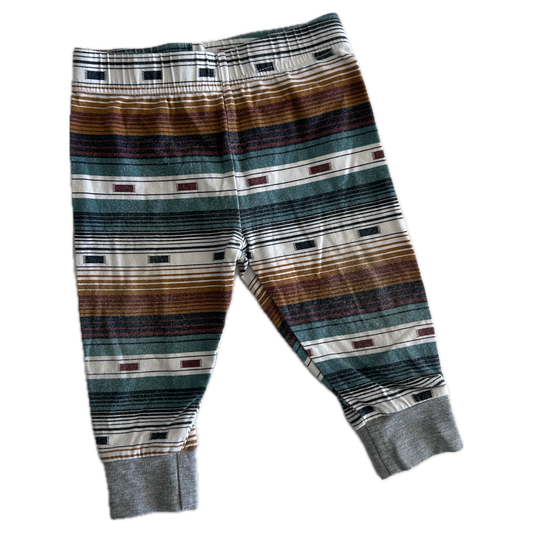 The front of pair of children's striped trousers with horizontal bands of brown, green, grey, black, and white, featuring ribbed ankle cuffs.