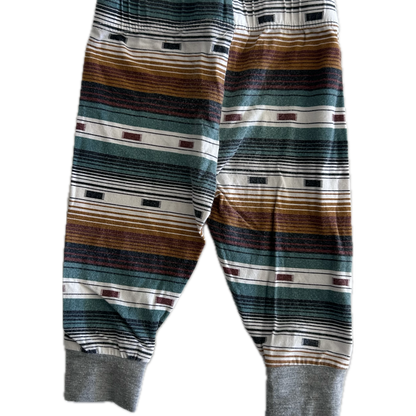 The back of pair of children's striped trousers with horizontal bands of brown, green, grey, black, and white, featuring ribbed ankle cuffs.