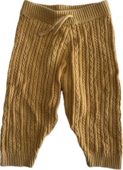 A pair of mustard yellow cable-knit baby pants with an elastic waistband and drawstring, shown against a plain white background.
