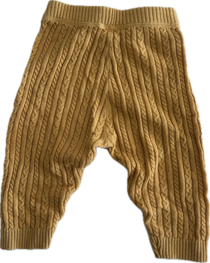 A pair of mustard yellow cable-knit baby pants with a wide elastic waistband and ribbed ankle cuffs, shown against a plain white background.