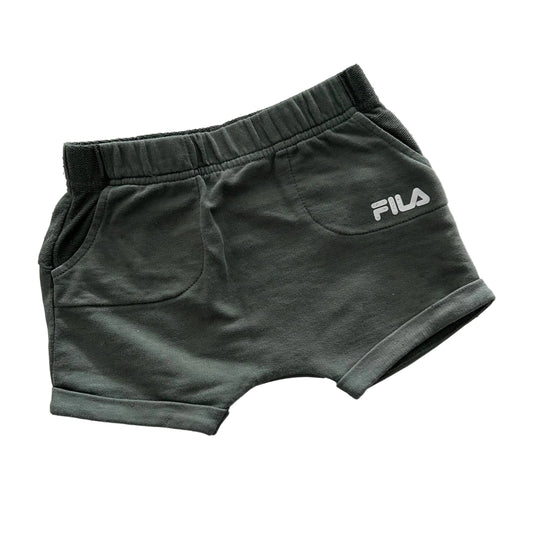A pair of dark olive green FILA shorts with a white logo on the side, laid flat on a white fabric background.