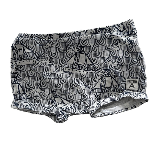 A pair of shorts with a navy blue and white wave and sailboat pattern, laid flat on a white fabric background.