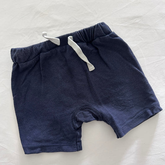 A pair of navy blue shorts with a white drawstring, laid flat on a white fabric background.