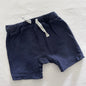 A pair of navy blue shorts with a white drawstring, laid flat on a white fabric background.