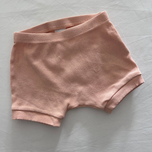 A salmon pink ribbed pair of baby shorts flat on a light fabric background.