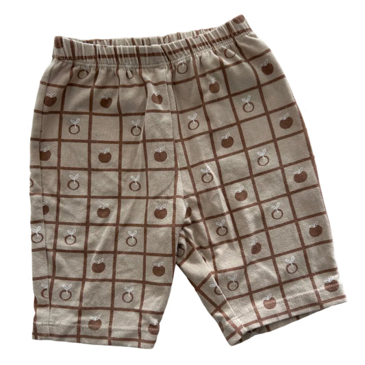 Light brown / tan shorts with dark brown grid lines and pictures of apples in opposite grids, photographed on a white background.