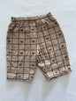 Light brown / tan shorts with dark brown grid lines and pictures of apples in opposite grids, photographed on a white background.