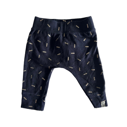 A pair of baby pants in dark navy blue with a scattered beige dash pattern, laid flat on a white fabric background.