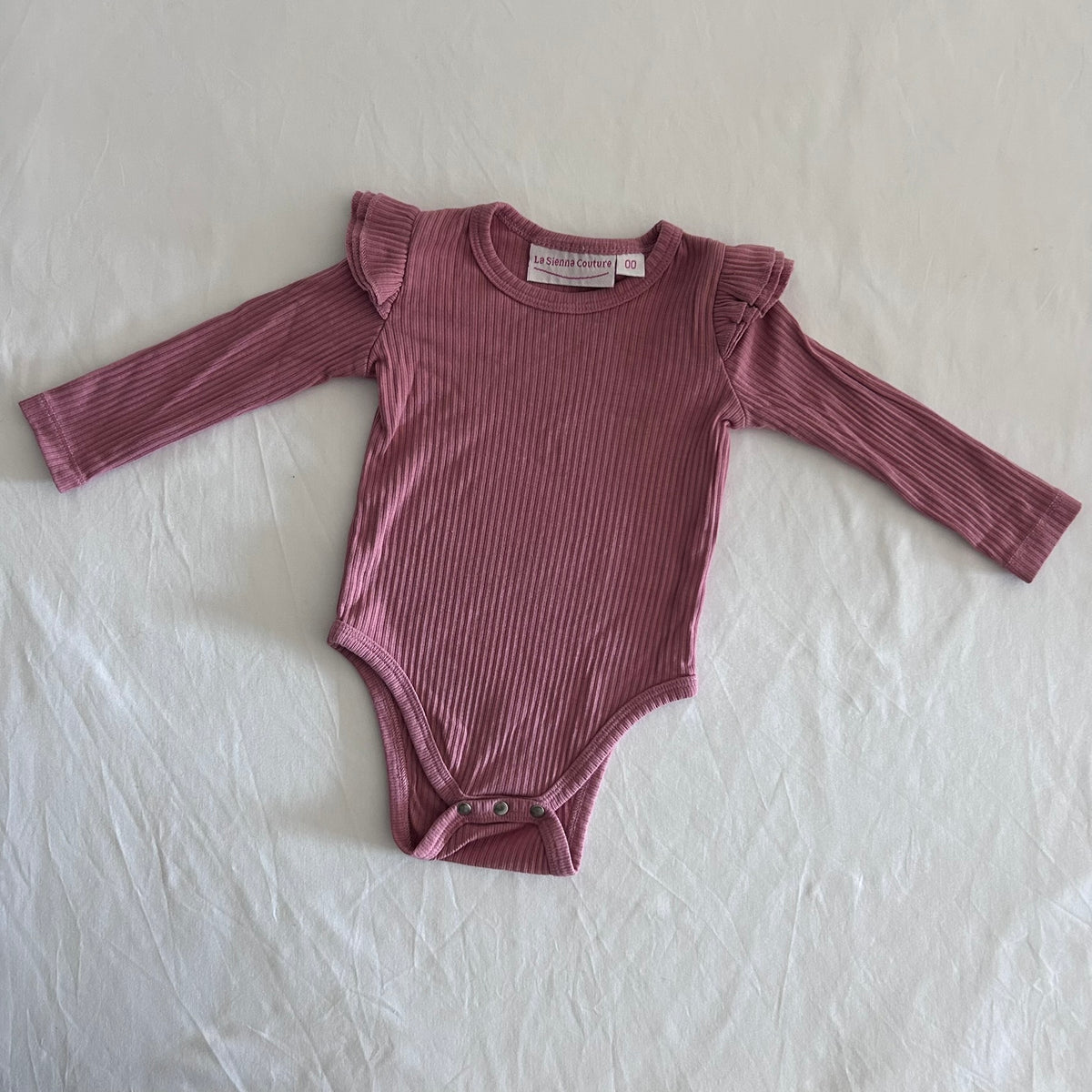 La Sienna Couture Age 00 long sleeve ribbed bodysuit in dusty pink with ribbed texture, frill/ruffle shoulder detail, gently loved condition.