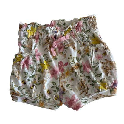 A pair of baby bloomers with a white background and a colorful print of bunnies, flowers, and bees, featuring a pink drawstring waist.