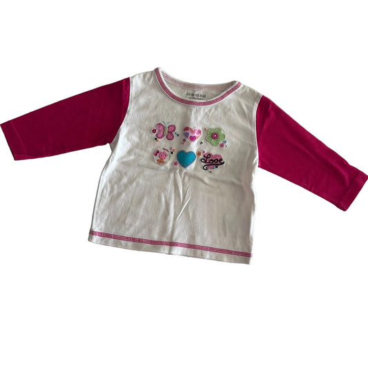 Okie dokie Age 1 long sleeved t-shirt in white and hot pink with embroidered and appliqué butterflies, flowers, heart, and 'love' text on front; pink contrast stitching at neckline and hem — like new condition.