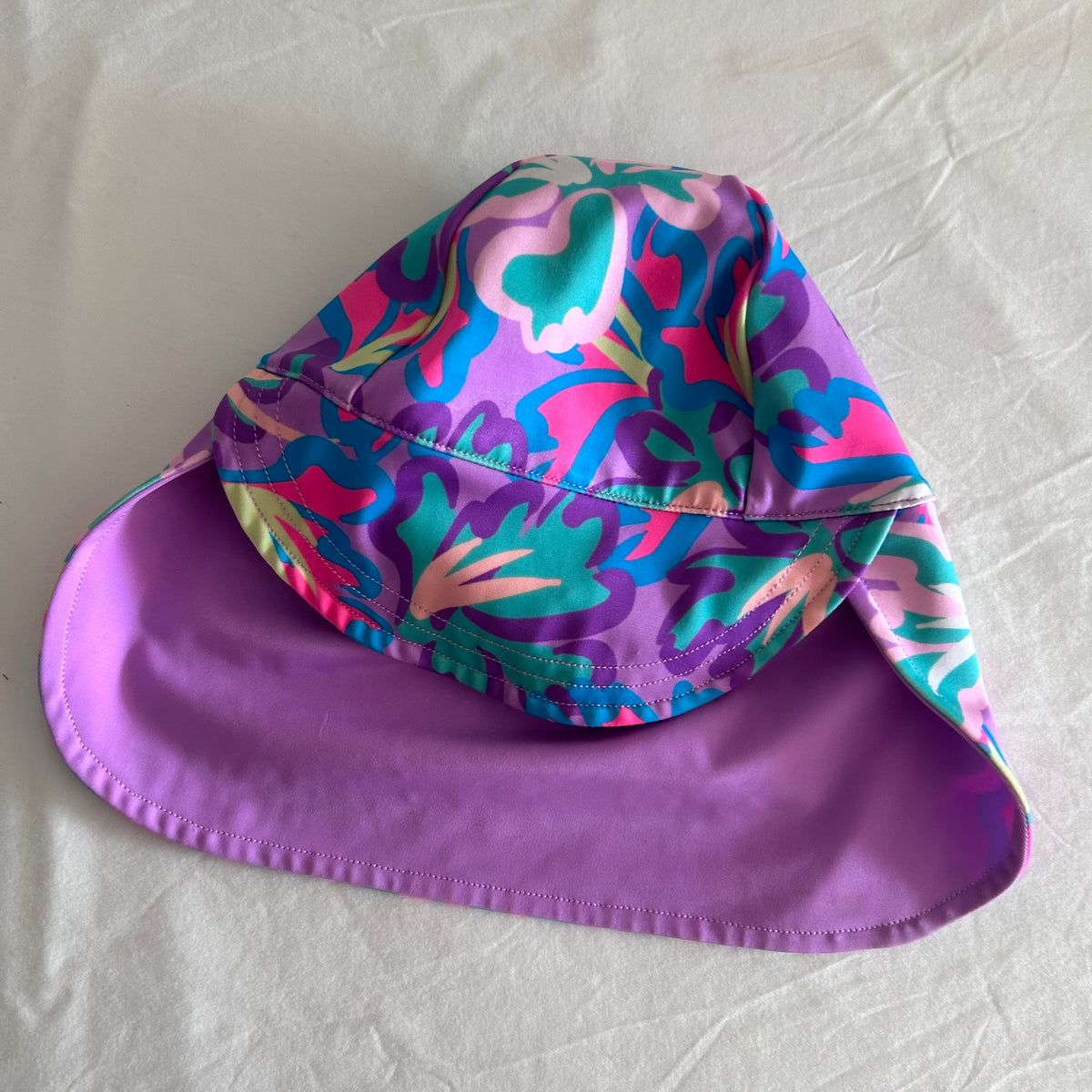 Bonds Age 0 swim sun hat with neck flap in purple, pink, teal, blue, yellow-green with abstract floral print on outer; solid lilac/purple on inner brim — like new condition.