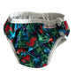 A reusable cloth diaper with a colorful dinosaur print on a dark green background, featuring white trim and snap closures, laid flat on a white fabric surface.