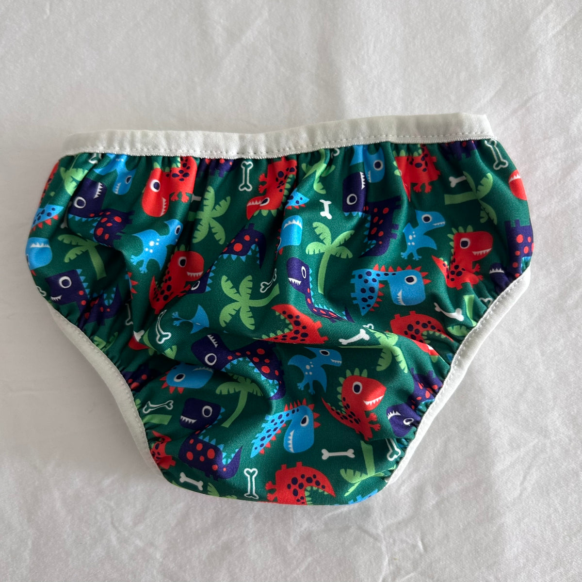 ImseVimse Age 1 reusable swim nappy in green, red, blue, purple, white with dinosaur and palm tree print — gently loved condition.