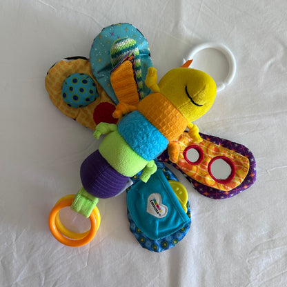 A colorful baby butterfly activity toy with a yellow plush head, patterned wings, and multiple sensory rings and fabric tabs, photographed on a white fabric background.